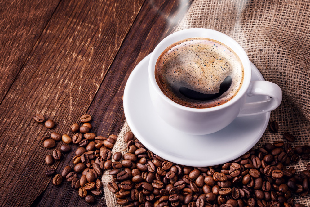 Tasse mit dampfendem Kaffee umgeben von Kaffeebohnen