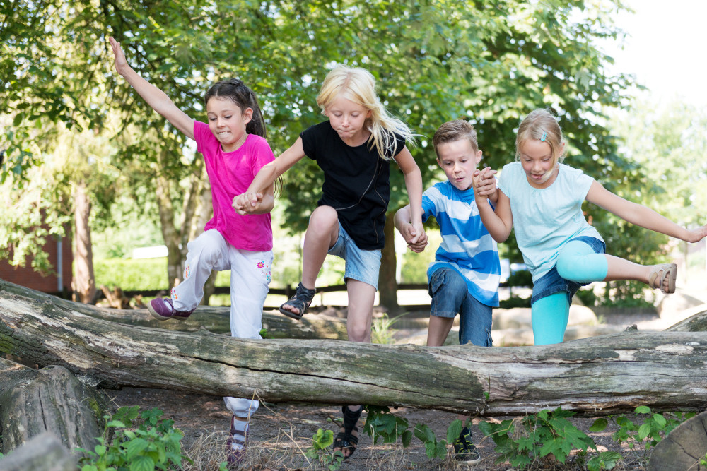 Vier Kinder springen über einen Baumstamm