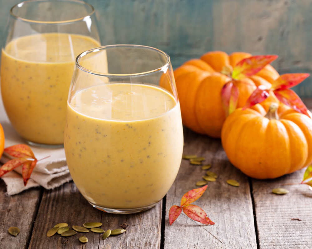 Zwei Gläser Kürbis-Smoothie mit Chiasamen, daneben zur Dekoration Hokkaidokürbisse mit verfärbtem Weinlaub.