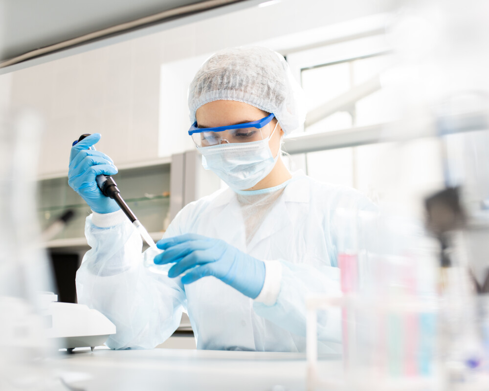 Frau mit Haarhaube, Mundschutz, Handschuhen und Kittel im Labor