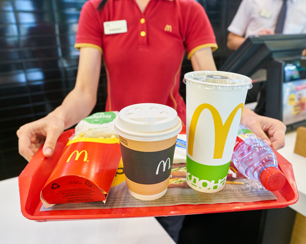 Mitarbeiterin von Mc Donalds reicht Tablett mit Menü über den Verkaufsstisch.