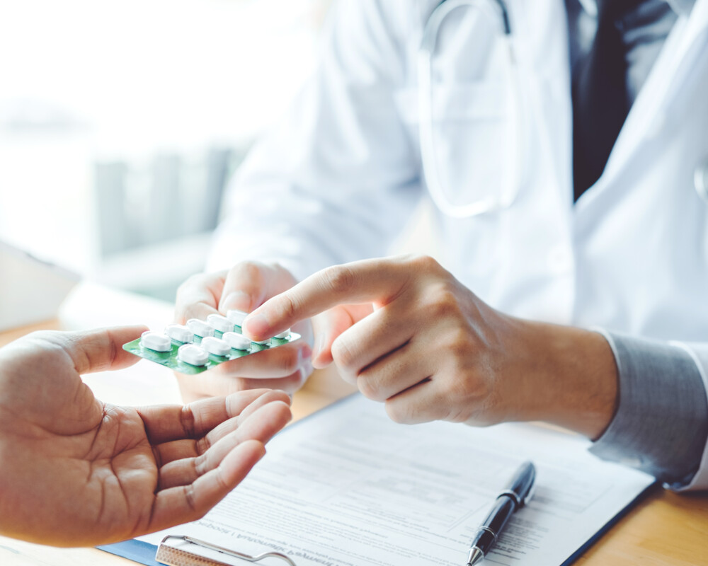 Arzt hält Patienten eine Blisterpackung mit Tabletten hin und zeigt darauf