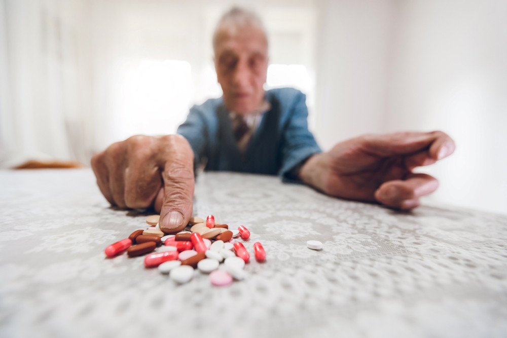 Senior zeigt auf einen Haufen von Medikamenten, die auf dem Tisch liegen