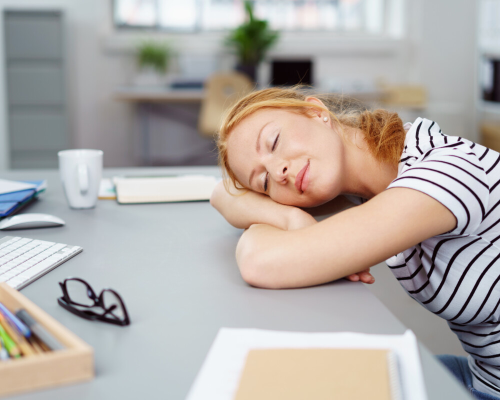 Frau schläft am Schreibtisch im Büro