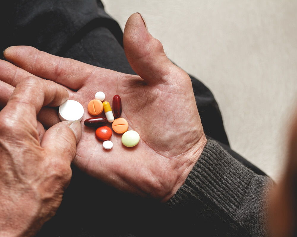 Hand einer älteren Person hält verschiedene Tabletten und Kapseln.
