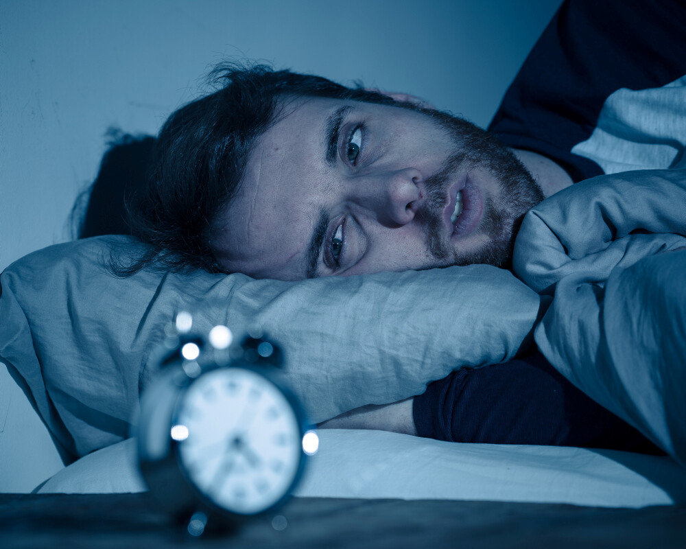 Symbolbild Schlafstörungen: Mann im Bett schaut auf Wecker. Symbolbild Schlafstörungen: Mann im Bett schaut auf Wecker.