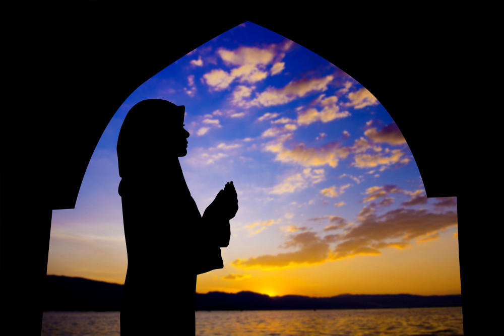 Silhouette einer muslimischen Frau, die während des Sonnenuntergangs in einer Moschee betet