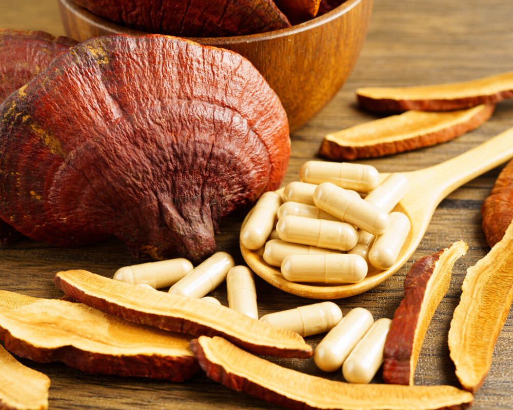 Reishi-Pilz und daneben Kapseln auf einem Löffel