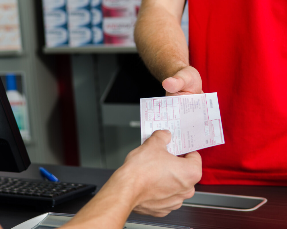 Kunde im roten T-Shirt reicht ein rosafarbenes Rezept über den HV-Tisch.