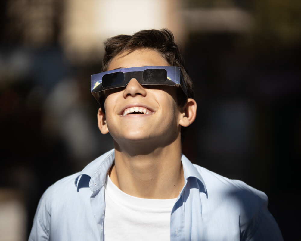 Junger Mann mit Sonnenschutzbrille betrachtet lächelnd die Sonnenfinsternis.