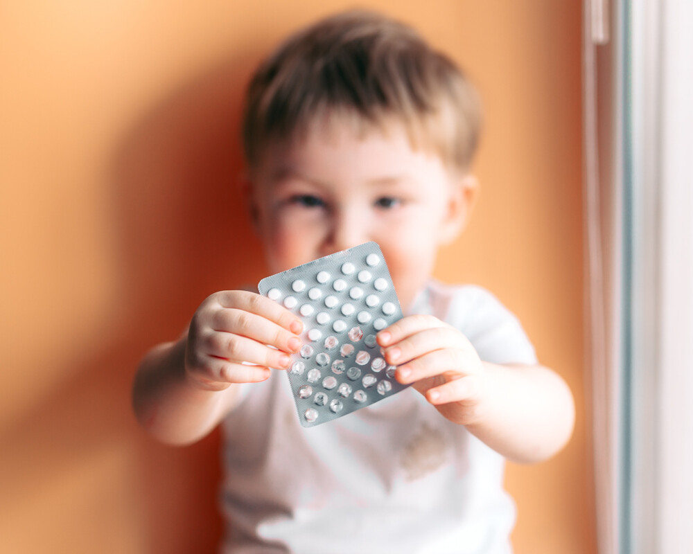 Ein Kleinkind hält einen Blister mit kleinen weißen Tabletten in den Händen.