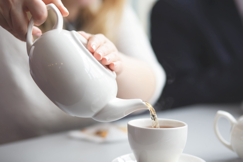 Frau schenkt Tee aus der Teekanne in eine Tasse