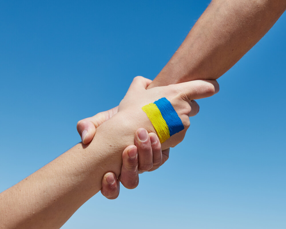 Zwei Hände greifen ineinander, ein Handrücken zeigt die Ukrainische Flagge.