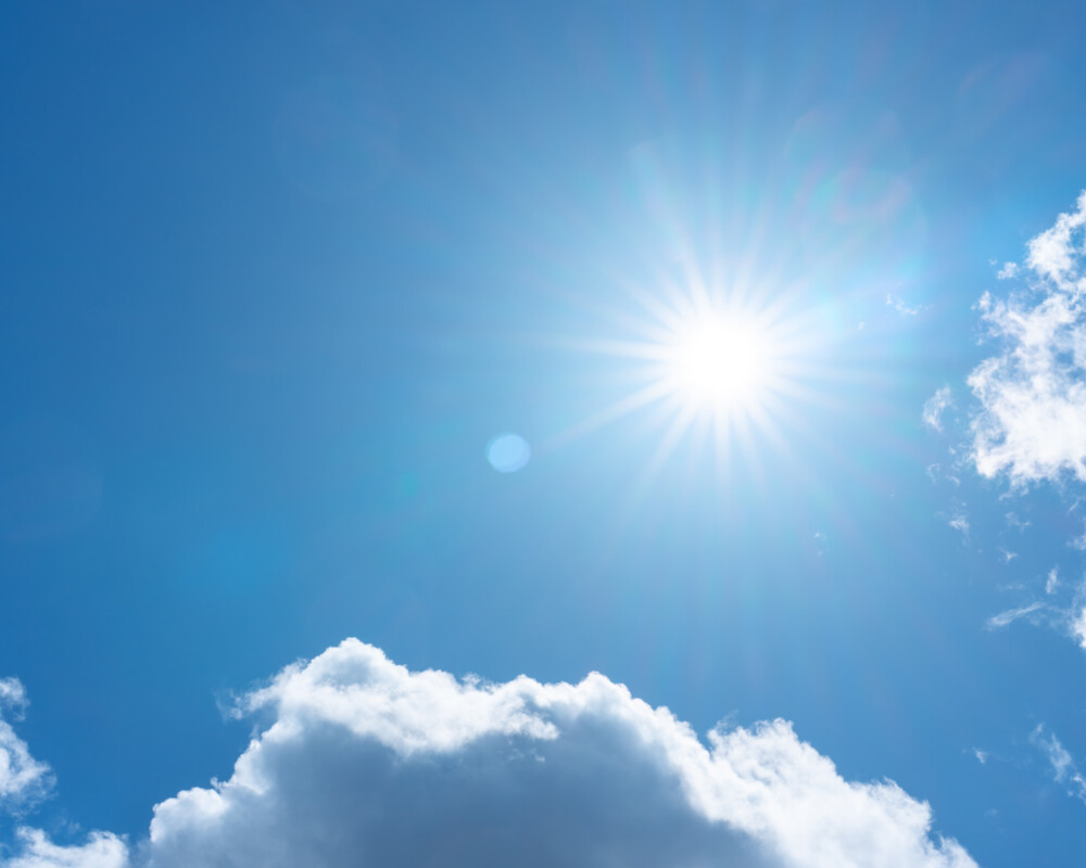 Blauer Himmel mit strahlender Sonne, wenig Wolken
