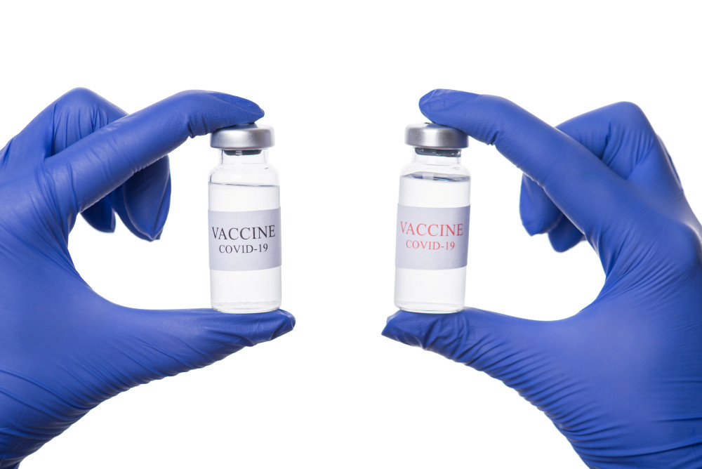 Zwei blau behandschuhte Hände halten jeweils ein Vial mit Aufschrift „Vaccine COVID-19