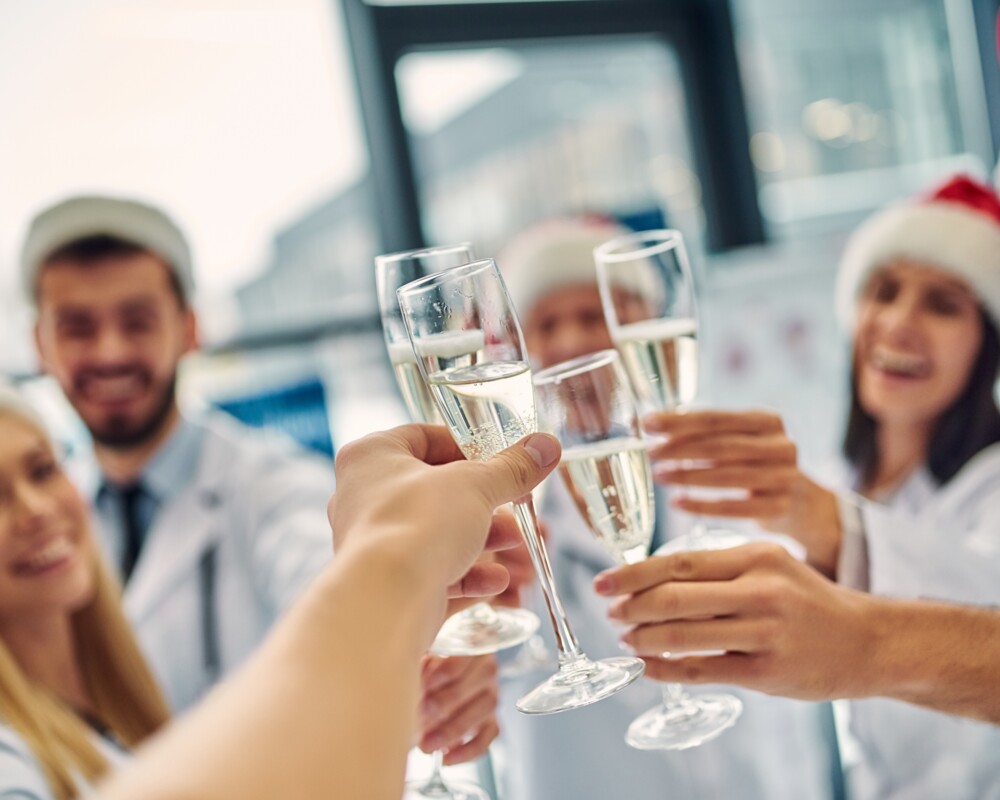 Gruppe von Frauen und Männern mit Weihnachtsmannmützen stößt mit Sektgläsern an.