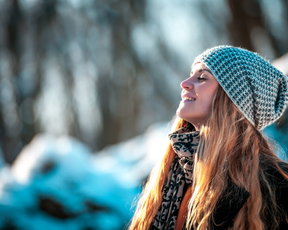 Junge Frau mit Mütze sonnt sich vor winterlichem Hintergrund.
