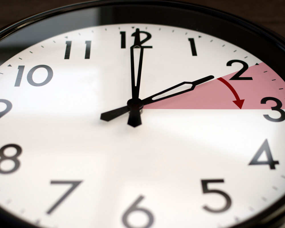 Uhr: Zeiger wird von 2 auf 3 Uhr vorgestellt – symbolisiert durch rotes Dreieck mit Pfeil in Richtung 3 Uhr.