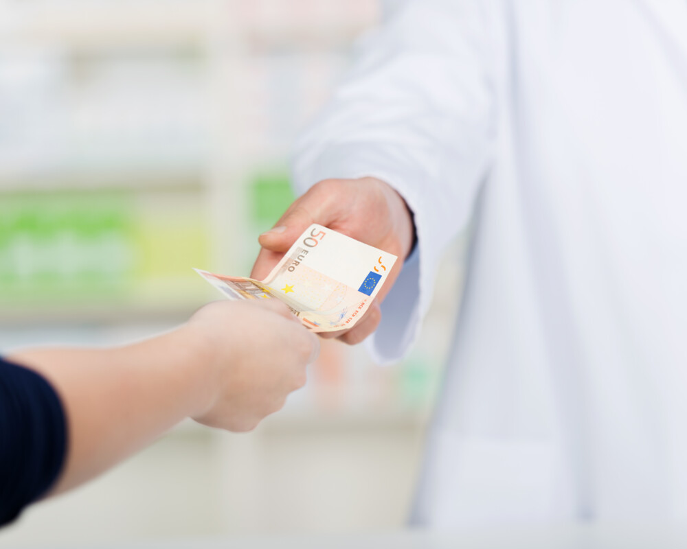 Kundin in der Apotheke reicht dem Apotheker einen 50-Euro-Schein.
