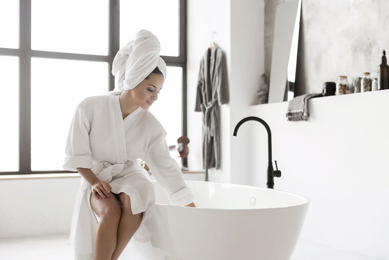 Frau im Bademantel sitzt auf dem Rand der Badewanne. Frau im Bademantel sitzt auf dem Rand der Badewanne.