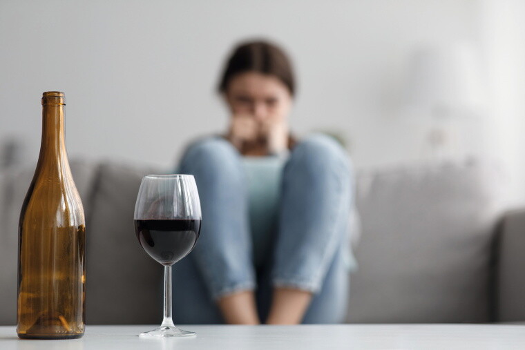 Vordergrund: Volles Weinglas
Hintergrund: Frau zusammengekauert auf dem Sofa Vordergrund: Volles Weinglas
Hintergrund: Frau zusammengekauert auf dem Sofa