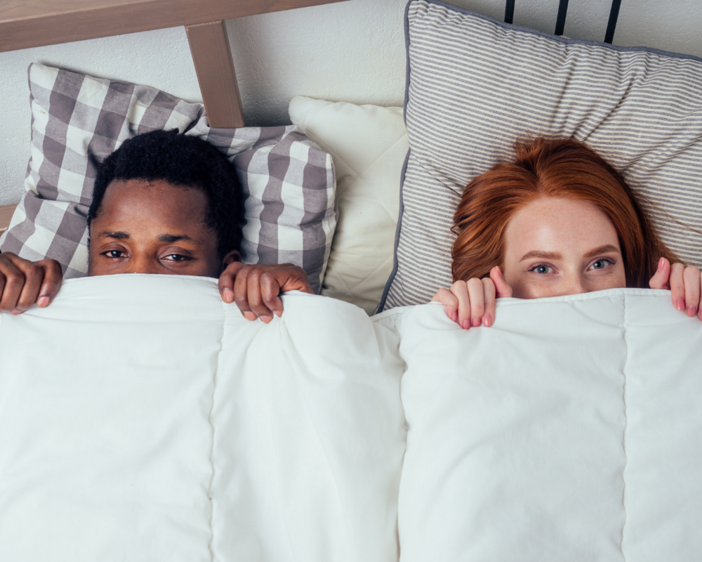 Mann und Frau ziehen sich Bettdecke bis unter die Augen