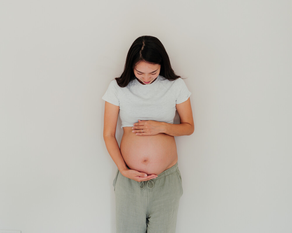 Schwangere Frau hält sich den unbedeckten Bauch.