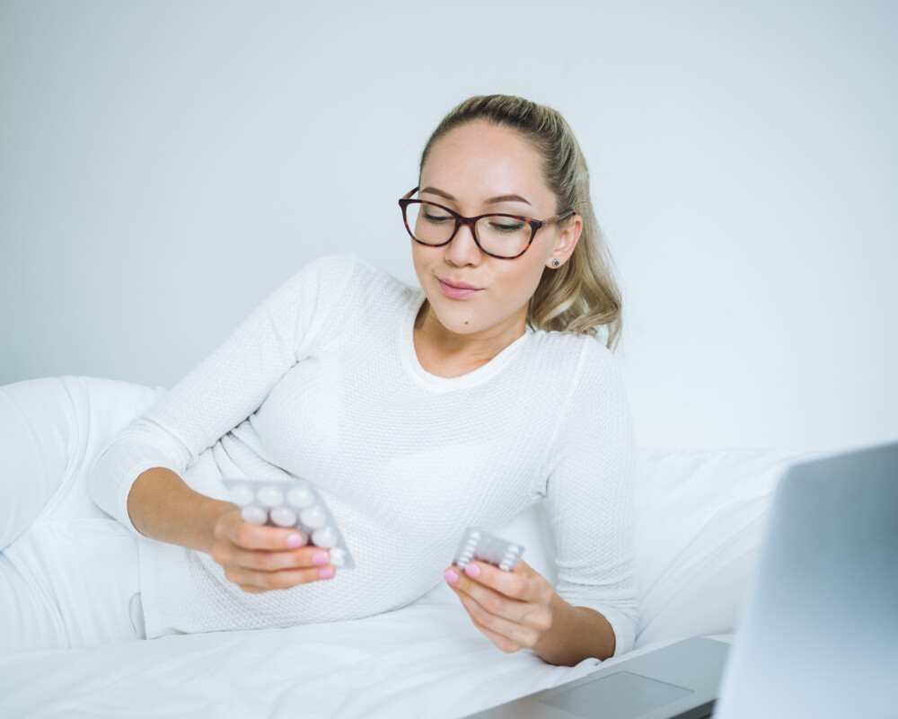 Frau liegt mit Vitamintabletten in den Händen auf dem Sofa Frau liegt mit Vitamintabletten in den Händen auf dem Sofa