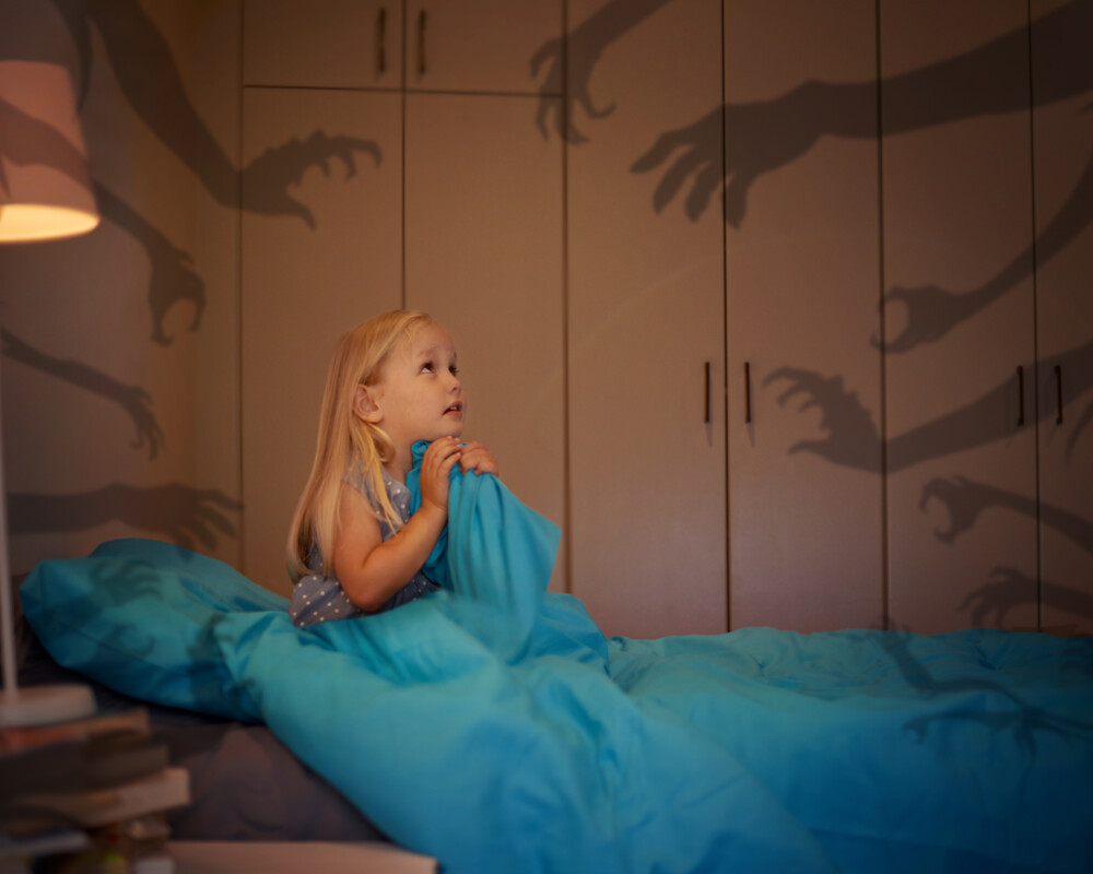 Kind im Bett, wach, Schattenhände symbolisieren Nachtschreck