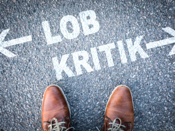Lob und Kritik auf dem Boden neben zwei Herrenschuhen