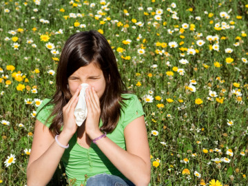 Jugendliche sitzt auf Blumenwiese und putzt sich die Nase
