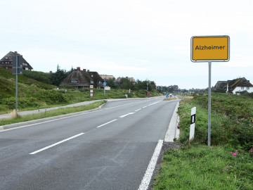 Leere Straße mit Ortsschild auf dem Alzheimer steht