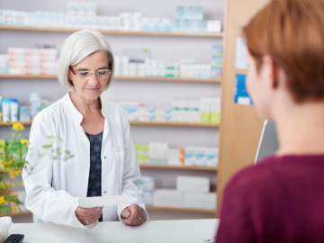 PTA/Apothekerin in der Offizin mit einem Rezept in der Hand