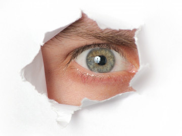 Auge schaut durch ein Loch im Papier