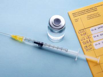Gelber Impfausweis mit drei Chargen-Etiketten und darüber liegender Spritze