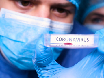 Mann mit Mundschutz hält Teströhrchen mit Aufschrift Coronavirus