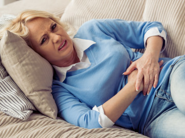Frau liegt mit Magenschmerzen auf dem Sofa