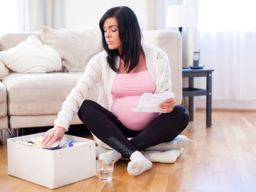 Schwangere sitzt auf dem Fußboden und liest einen Beipackzettel