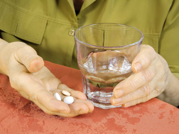 Alte Frau mit drei Tabletten und Wasserglas.