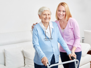 Alte Dame am Rollator wird von junger Frau umarmt