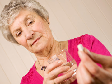 Frau mit einem Glas Wasser in der Hand blickt skeptisch auf eine Tablette