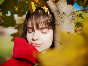 Frau steht mit geschlossenen Augen unter einem Baum