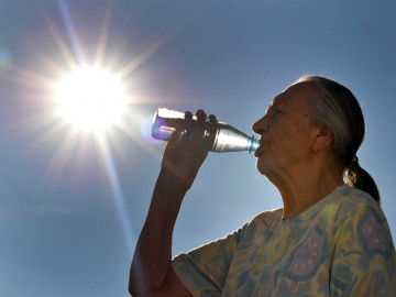 Frau trinkt Mineralwasser aus der Flasche. Die Sonne scheint gleißend.