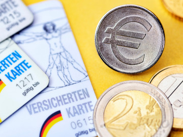 Versichertenkarten neben Euromünzen