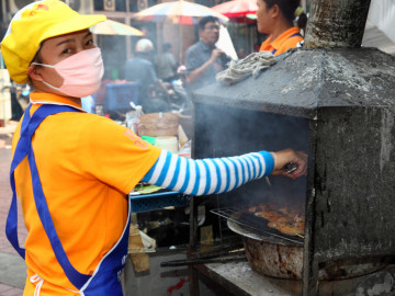Chinesische Frau mit Atemmaske am Grill