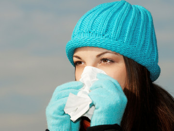 Junge Frau mit Mütze und Handschuhen putzt sich die Nase