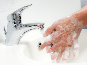 Eingeseifte Hände, die über einem Waschbecken unter den Wasserstrahl gehalten werden.