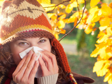Junge Frau im herbstlichen Ambiente, putzt sich die Nase