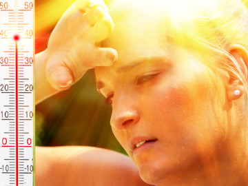 Thermometer zeigt 40 °C. Frau wischt sich Schweiß von der Stirn