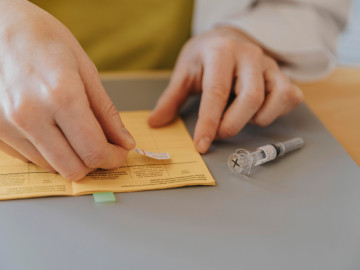 Doktor klebt Aufkleber in gelben Impfpass.